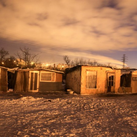 Nighttime scene of a row of shacks blanketed in snow, with soft moonlight casting shadows