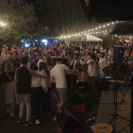 Na zewnątrz, w świetle lampionów, nocą tańczą ludzie, niektórzy grają na instrumentach. Na scenie stoją dwaj muzycy odwróceni tyłem.