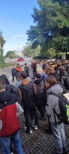 Grupowe zdjęcie nastolatków podczas spaceru z drzewami, niebieskim niebem oraz innymi ludźmi w oddali