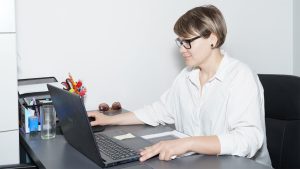 Kobieta w okularach jest pochłonięta pracą na swoim laptopie, otoczona schludnym biurkiem i miękkim oświetleniem.