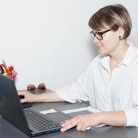 Kobieta w okularach jest pochłonięta pracą na swoim laptopie, otoczona schludnym biurkiem i miękkim oświetleniem.