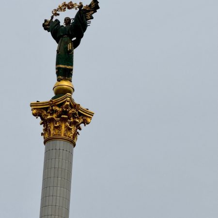 A woman’s statue stands proudly on a column, symbolizing strength and beauty on the grey sky background
