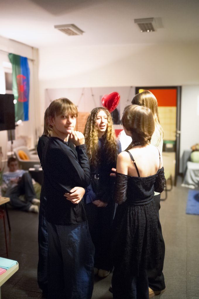 A group of girls wearing black standing in a bright room, interacting and laughing together in a friendly atmosphere.