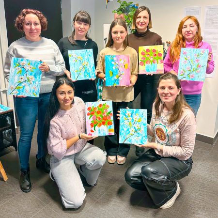 A group of women holding their paintings, smiling and proud of their artworks.