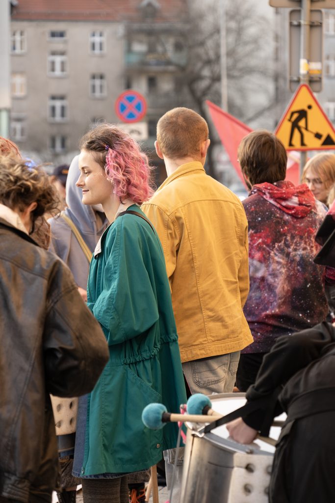 A diverse group of people gathered in the background engaged in conversation and enjoying each other's company, in the foreground there is large metal drum.