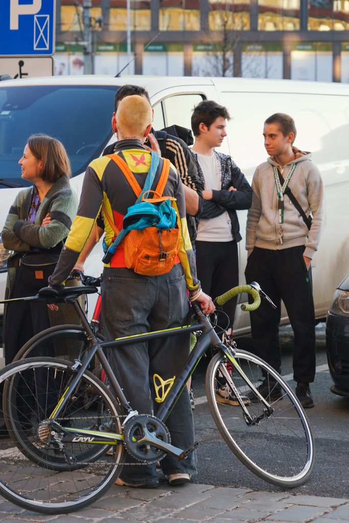 A man standing next to his bike, more people in the background and white bus behind them