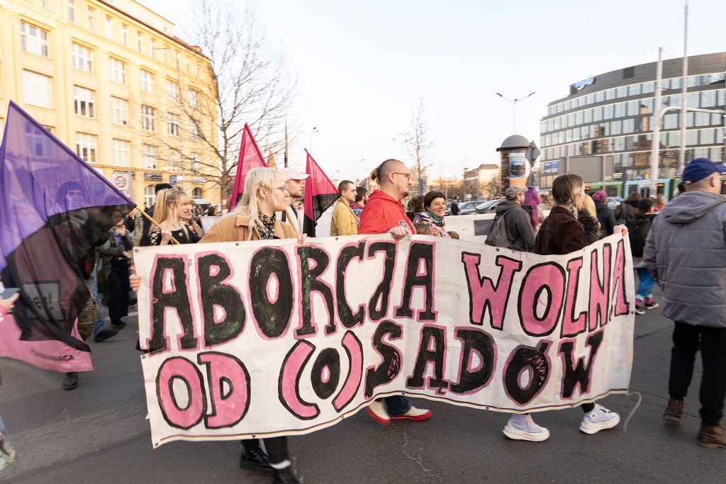 People walk together down the street, holding a banner that says "Abortion free from judgment."
