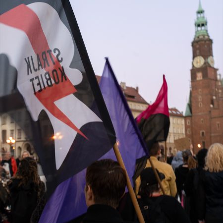 A diverse group of people proudly holding a flag featuring an image of a woman's strike, showcasing unity and support.