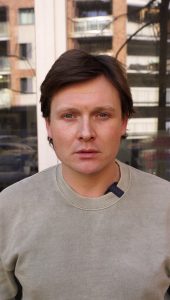 Mężczyzna w casualowym ubraniu, stoi na tle zielonego parku.