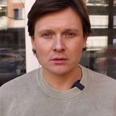 Mężczyzna w casualowym ubraniu, stoi na tle zielonego parku.