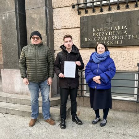 Three people are standing in front of the building of the Human Rights Office of the Republic of Poland, holding a sheet of paper in their hands